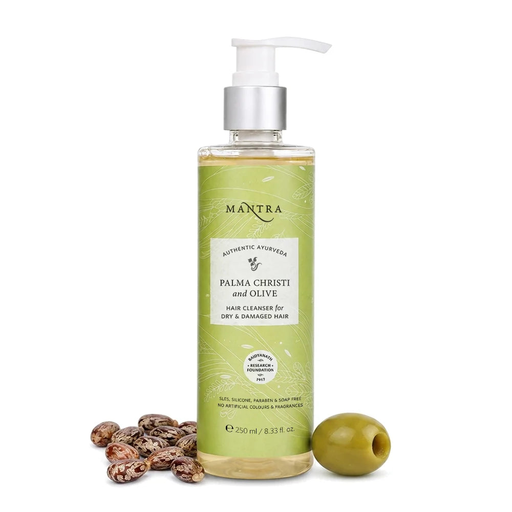 A bottle of Mantra Palma Christi and Olive hair cleanser with a white pump dispenser, shown on a white background with whole olives and palm kernels at the base.