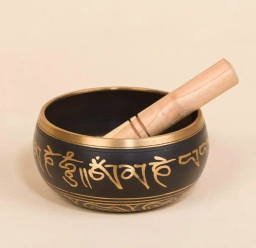 Black singing bowl with gold script and wooden striker on a beige background