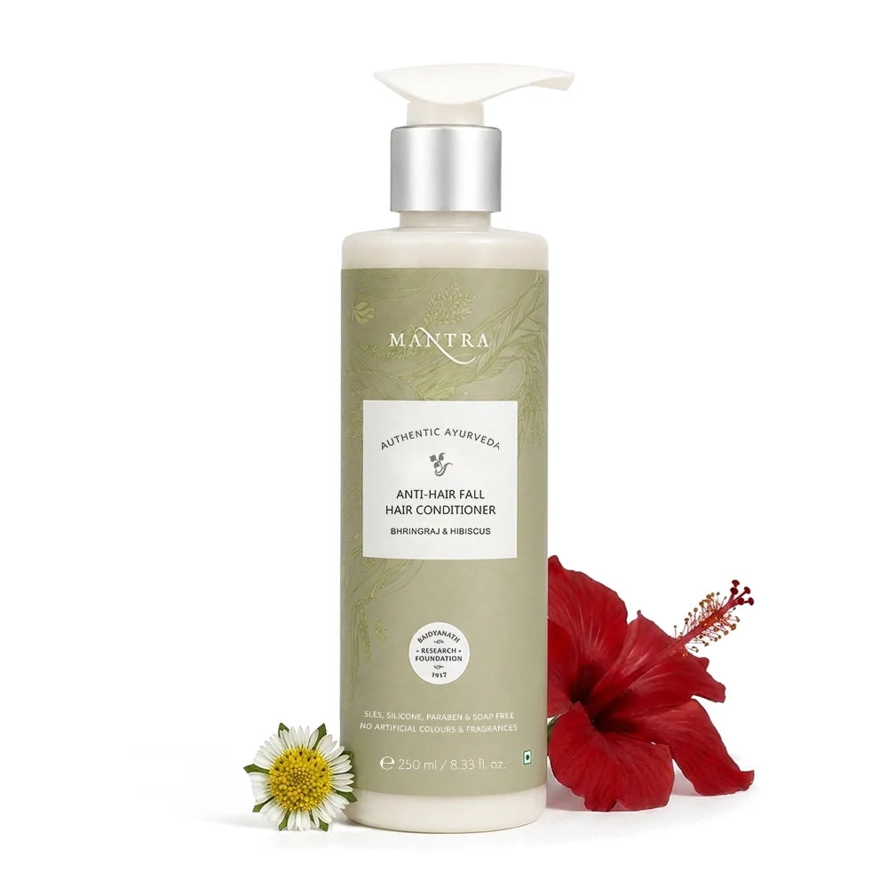 A bottle of Mantra Authentic Ayurveda Anti-Hair Fall Hair Conditioner, styled with a red hibiscus flower and a small white daisy on a clean white background.
