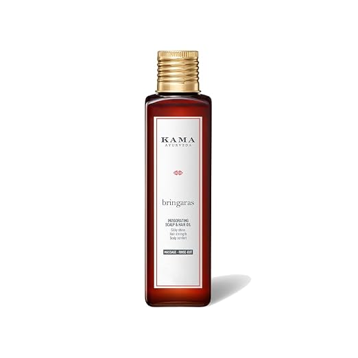 A bottle of Kama Ayurveda Bringaras Resurfacing Hair & Hair Oil in a dark amber glass bottle with a gold cap and a white label, shown on a white background with a soft shadow.
