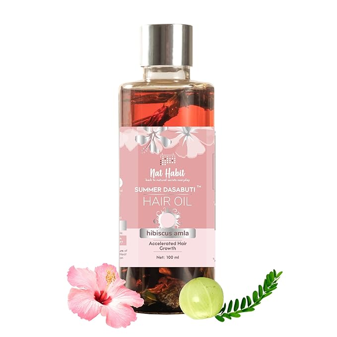 Hair oil bottle with pink label featuring hibiscus and amla, surrounded by flowers and leaves on a white background.